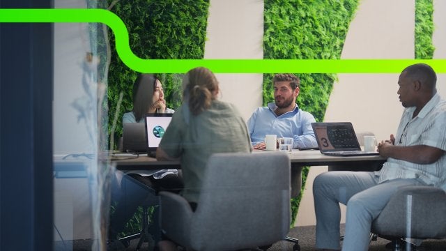 Equipo corporativo en reunión estratégica frente a un muro verde vegetal, conversando sobre sostenibilidad y decisiones empresariales.